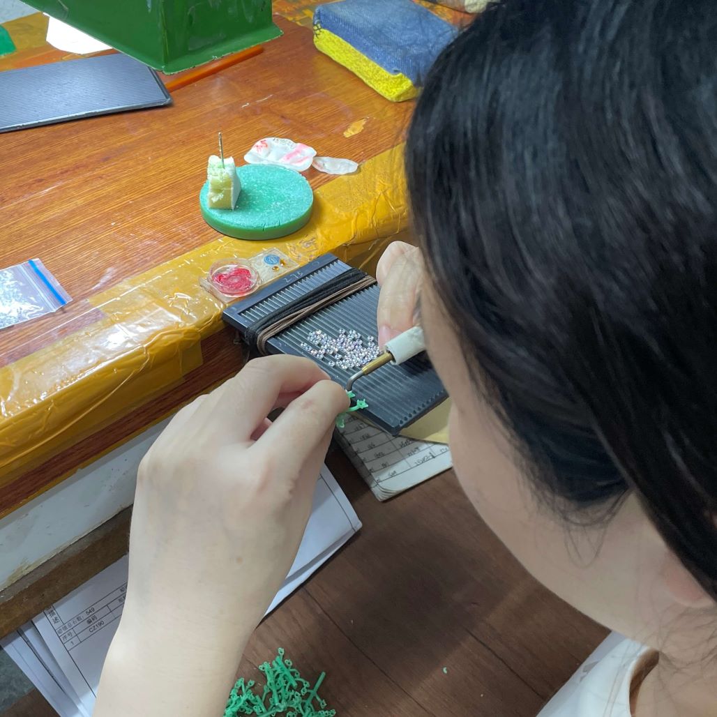 Craftsman performing hand wax‑inlay gemstone setting in jewelry factory workshop